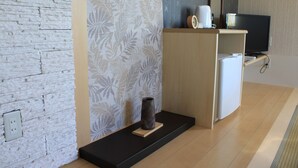 A modern room with a stone-textured wall, a decorative panel with a leaf pattern, a small black table with a vase, a white refrigerator, and a television on a wooden stand. - Petit Hotel Blanc Fleur (Nakafurano)