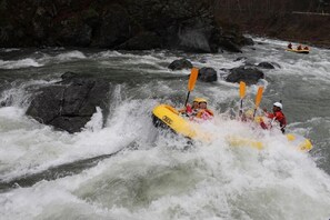 A group of people in a yellow raft navigating a river with rapids. - Petit Hotel Blanc Fleur (Nakafurano)