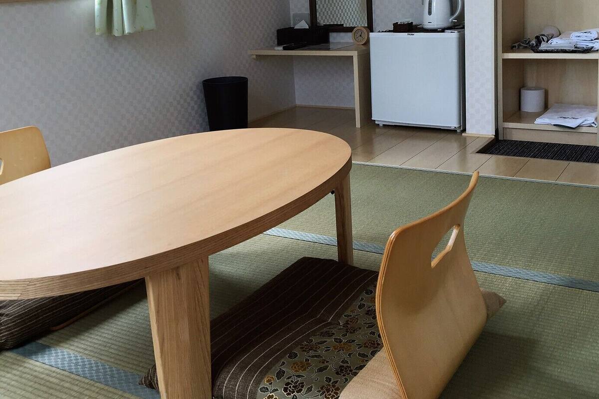 Een compacte, moderne kamer met een houten eettafel, een enkele stoel, een kitchenette en een raam met gordijnen.