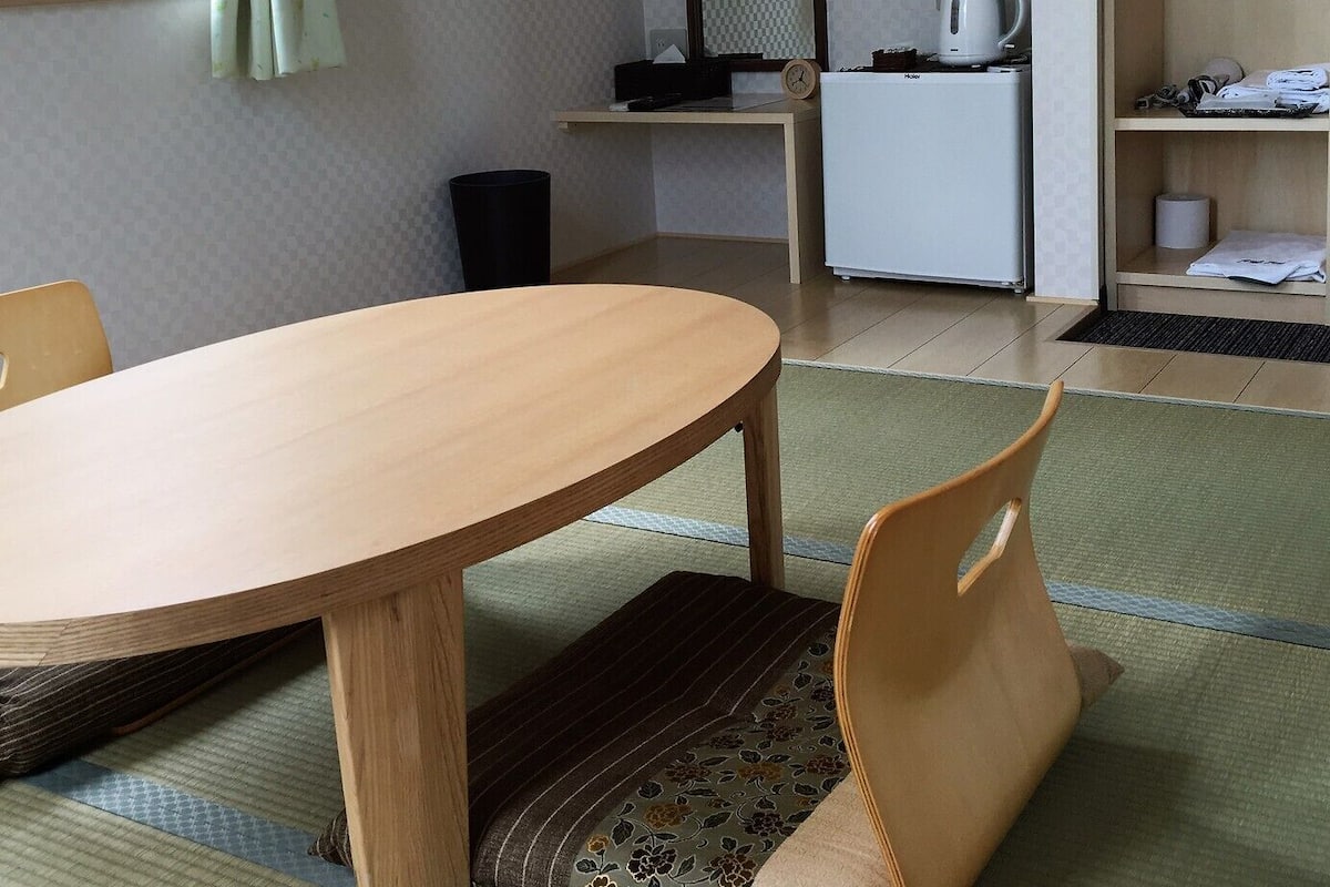 Quarto pequeno e moderno com mesa de jantar de madeira, uma cadeira, cozinha compacta e janela com cortinas.