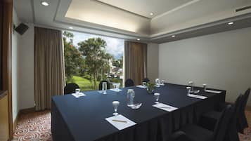 Une salle de conférence avec une longue table, des chaises et une vue sur un jardin grâce à de grandes fenêtres.