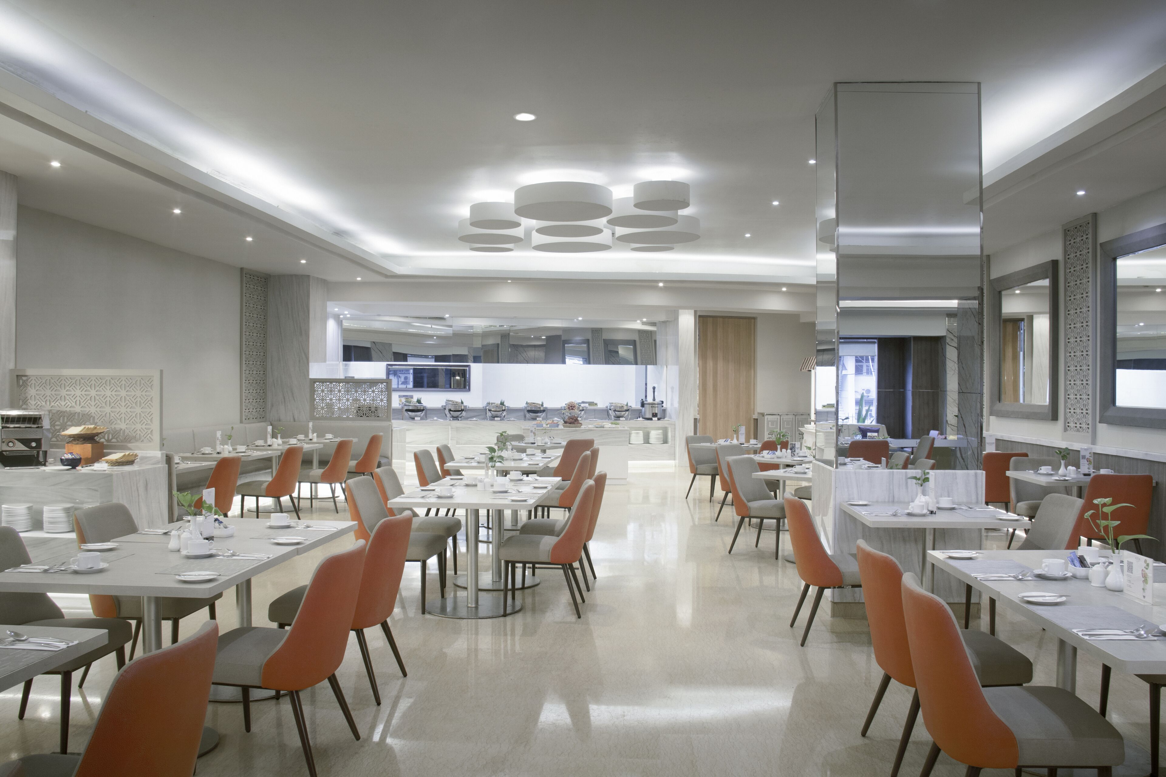 Un comedor moderno con varias mesas y sillas, una cocina al fondo y un ambiente limpio y bien iluminado.
