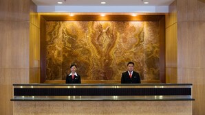 A reception desk with two staff members, a marble wall, and wooden paneling. - Aston Manado Hotel (Manado)
