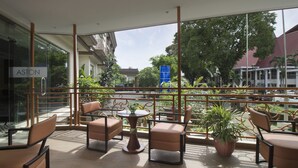 A balcony with seating and potted plants, overlooking a street with buildings and trees. - Aston Manado Hotel (Manado)