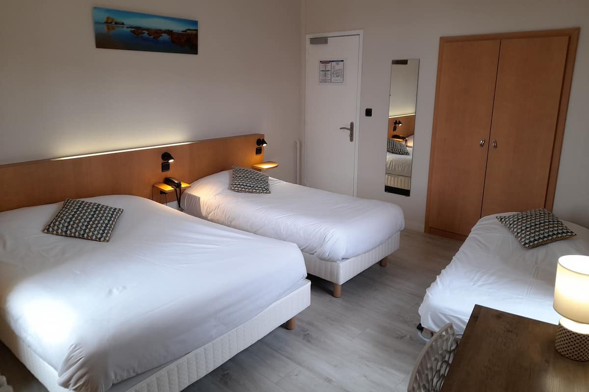 A hotel room with two single beds, a wooden wardrobe, a nightstand with a lamp, and a painting on the wall.