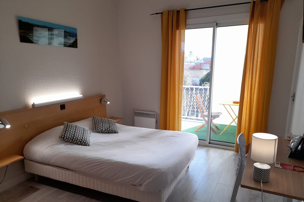 A hotel room with a large bed, a bedside table, a lamp, and a view of the outdoor area.