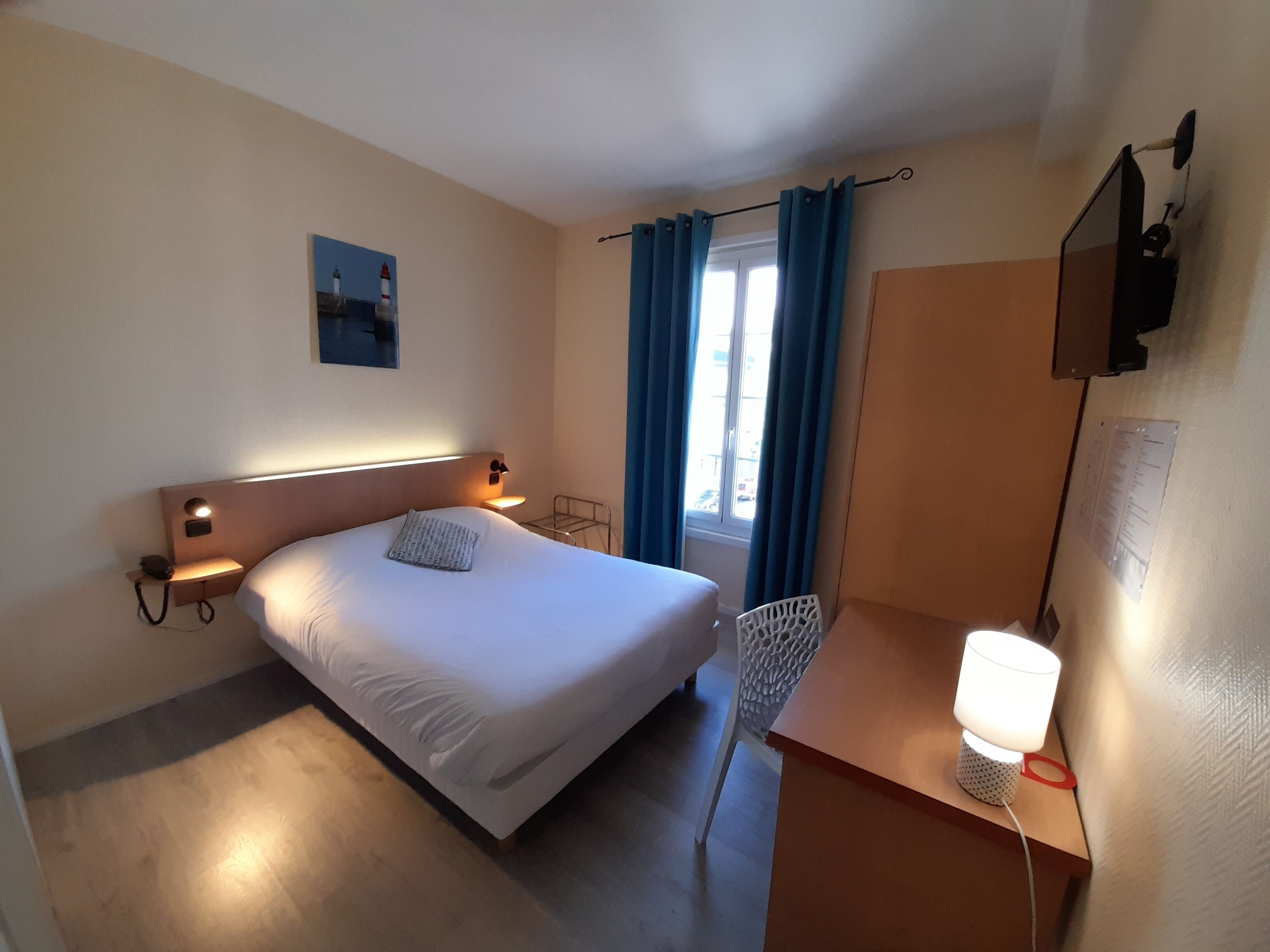 Habitación de hotel con cama, lámparas de noche, escritorio con lámpara, una silla y ventana con cortinas.