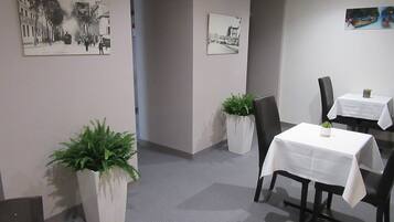 Un salón de conferencias con una mesa, sillas, plantas en macetas y cuadros en las paredes.