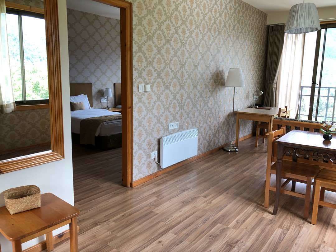 Ein Hotelzimmer mit Holzboden, einem Bett mit weißen Leinentüchern, einem Schreibtisch mit Lampe und einem Esstisch mit Stühlen.