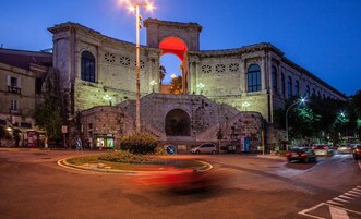 Un edificio histórico con un arco destacado, una glorieta y una calle con coches.