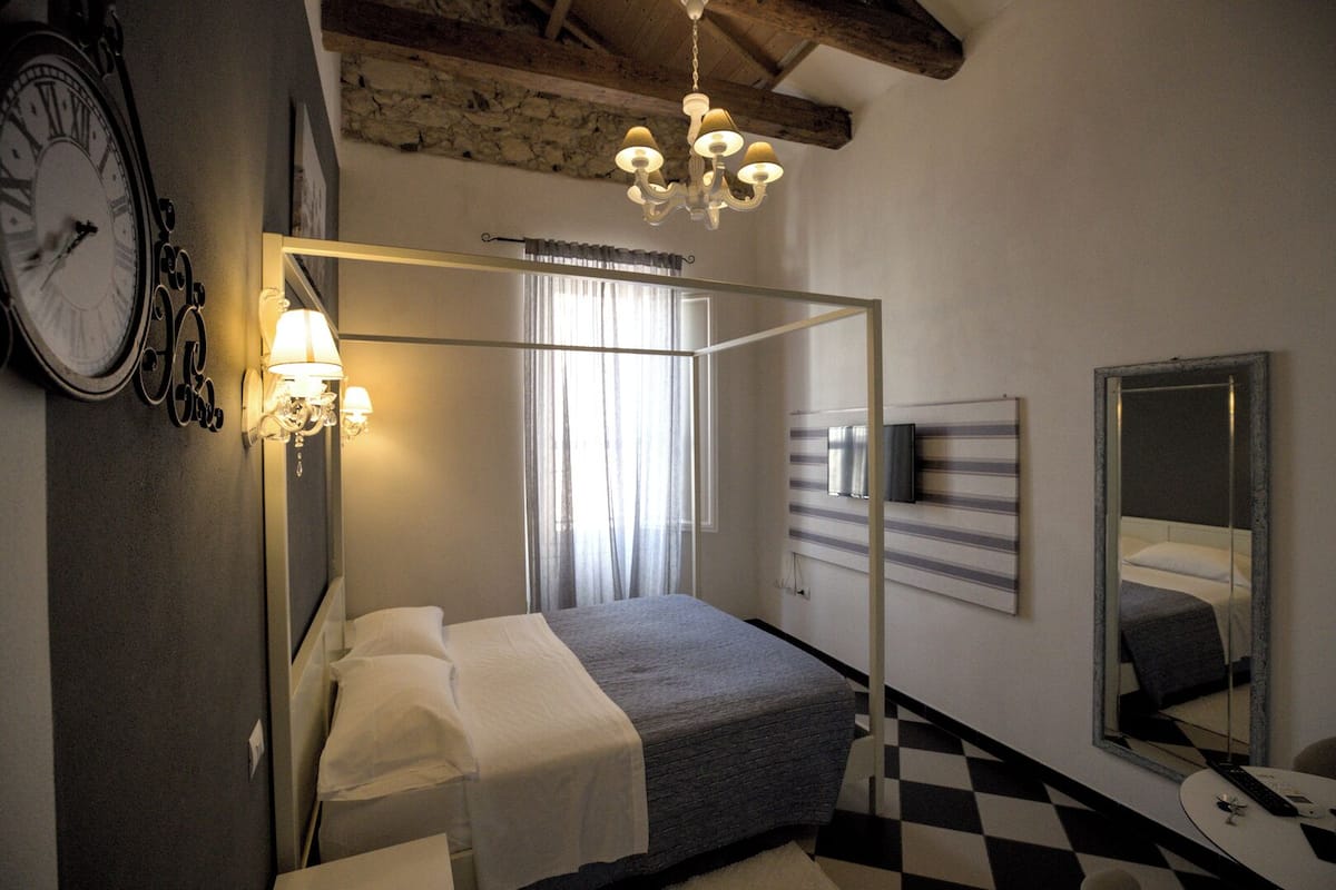 A bedroom with a four-poster bed, a large wall clock, a chandelier, and a checkered floor.