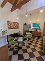 Una cocina moderna con piso a cuadros, un refrigerador, un lavamanos y un espejo. Hay lámparas colgantes y una obra de arte colorida en la pared.