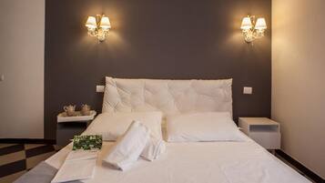 Una cama bien hecha con sábanas y almohadas blancas, dos mesitas de noche con lámparas, y un piso a cuadros.