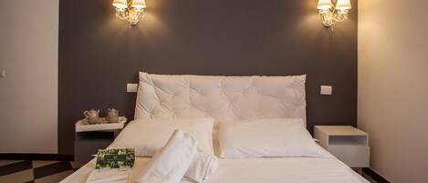 Una cama bien hecha con sábanas y almohadas blancas, dos mesitas de noche con lámparas, y un piso a cuadros.