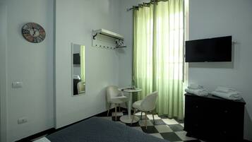 Ein Hotelzimmer mit Bett, Schreibtisch mit Stuhl, Fernseher, Spiegel, einer Uhr und einem Fenster mit Vorhängen.