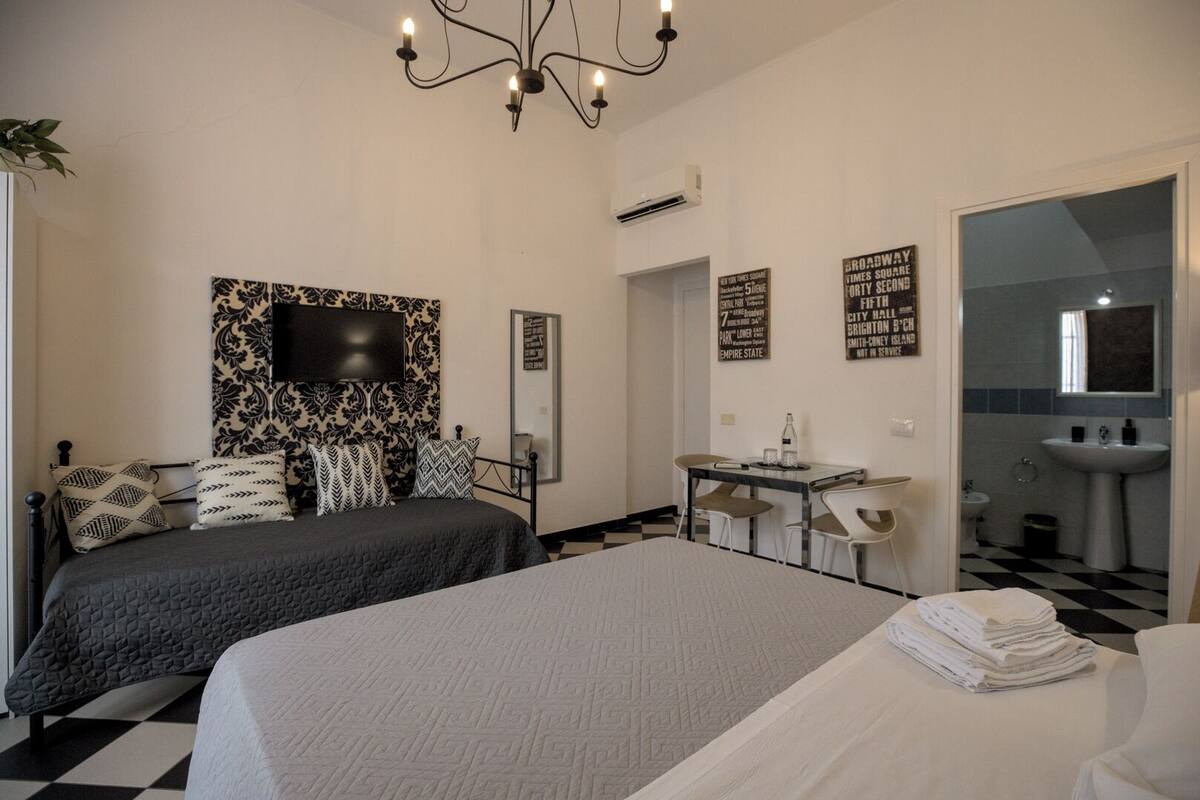 A hotel room with two beds, a desk, a chair, a TV, and a bathroom.