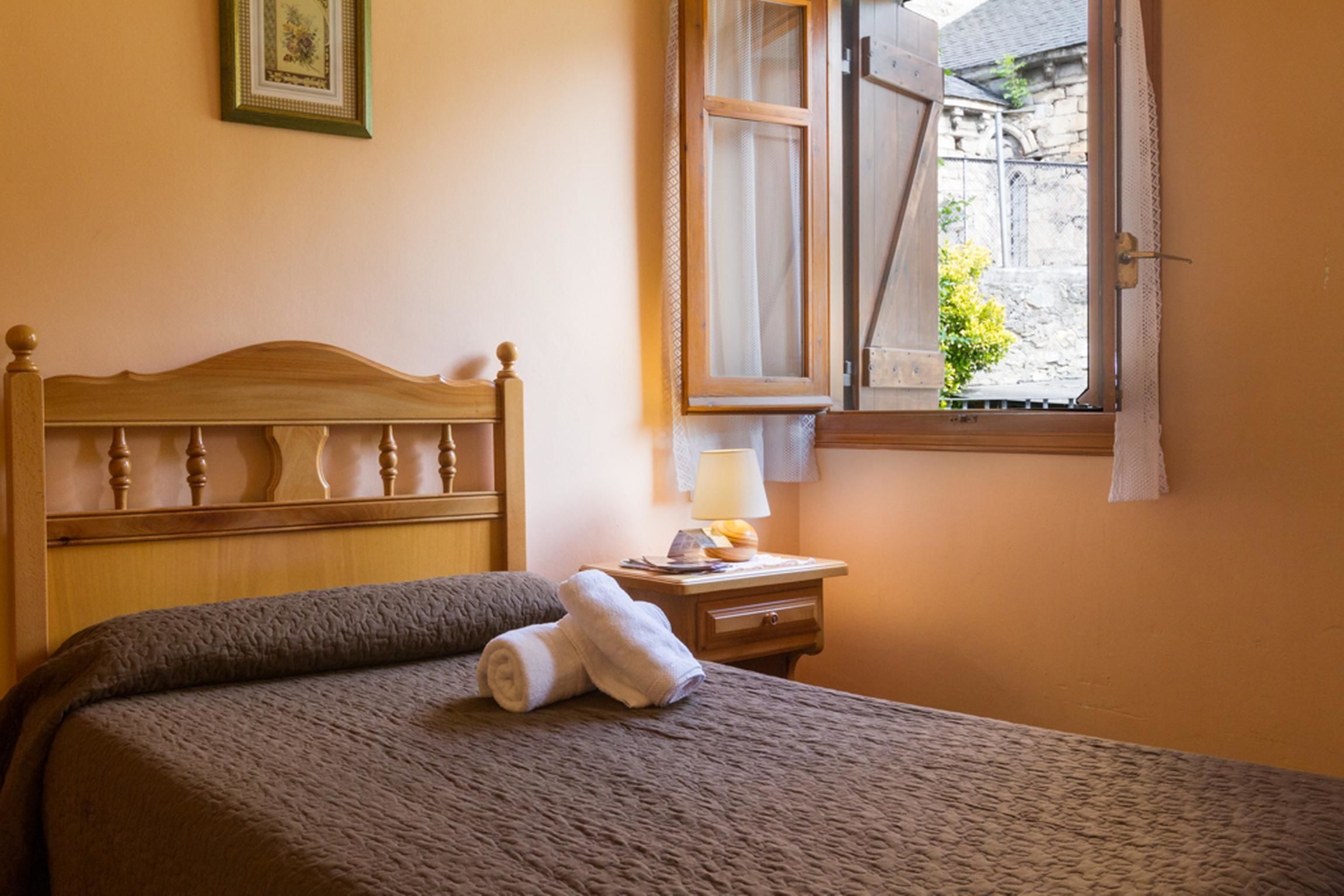 A neatly made bed with a headboard, a bedside table with a lamp, and a window with curtains.