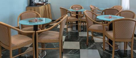 Un comedor con mesas redondas, sillas de mimbre, una estación de café y un piso con estampado de cuadros.