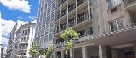 A multi-story building with balconies, parked cars, and a clear sky.