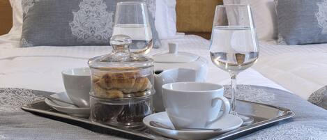 A tray with a coffee pot, cups, and glasses on a bed with pillows and a blanket.