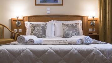 A neatly made bed with a quilted cover, two decorative pillows, and rolled towels on the side.