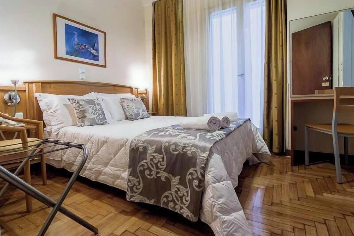A neatly made bed with a patterned bedspread, a wooden nightstand with a lamp, and a chair.