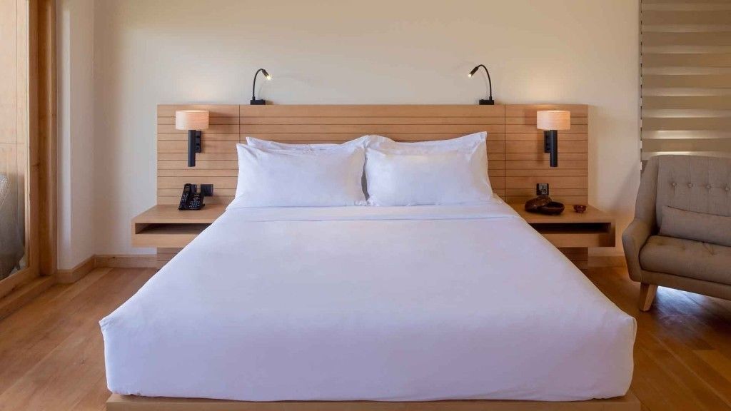 A large bed with white linens, two bedside tables with lamps, and a chair.