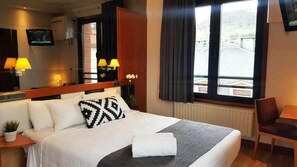 Une chambre d’hôtel avec un lit, un bureau, une chaise, une télévision et une fenêtre avec des rideaux.