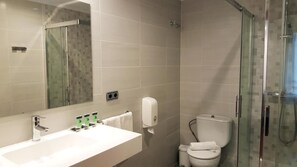 Une salle de bain moderne avec une douche à parois de verre, un lavabo blanc avec un miroir et des toilettes.
