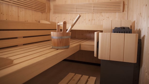 Una sauna con bancos de madera, un cubo de madera con un cepillo y un calentador.