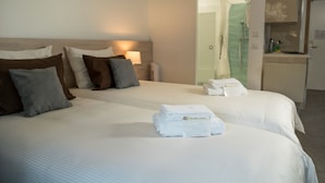 Habitación de hotel con dos camas, una mesita de noche, una lámpara y un baño visible a través de una puerta abierta.