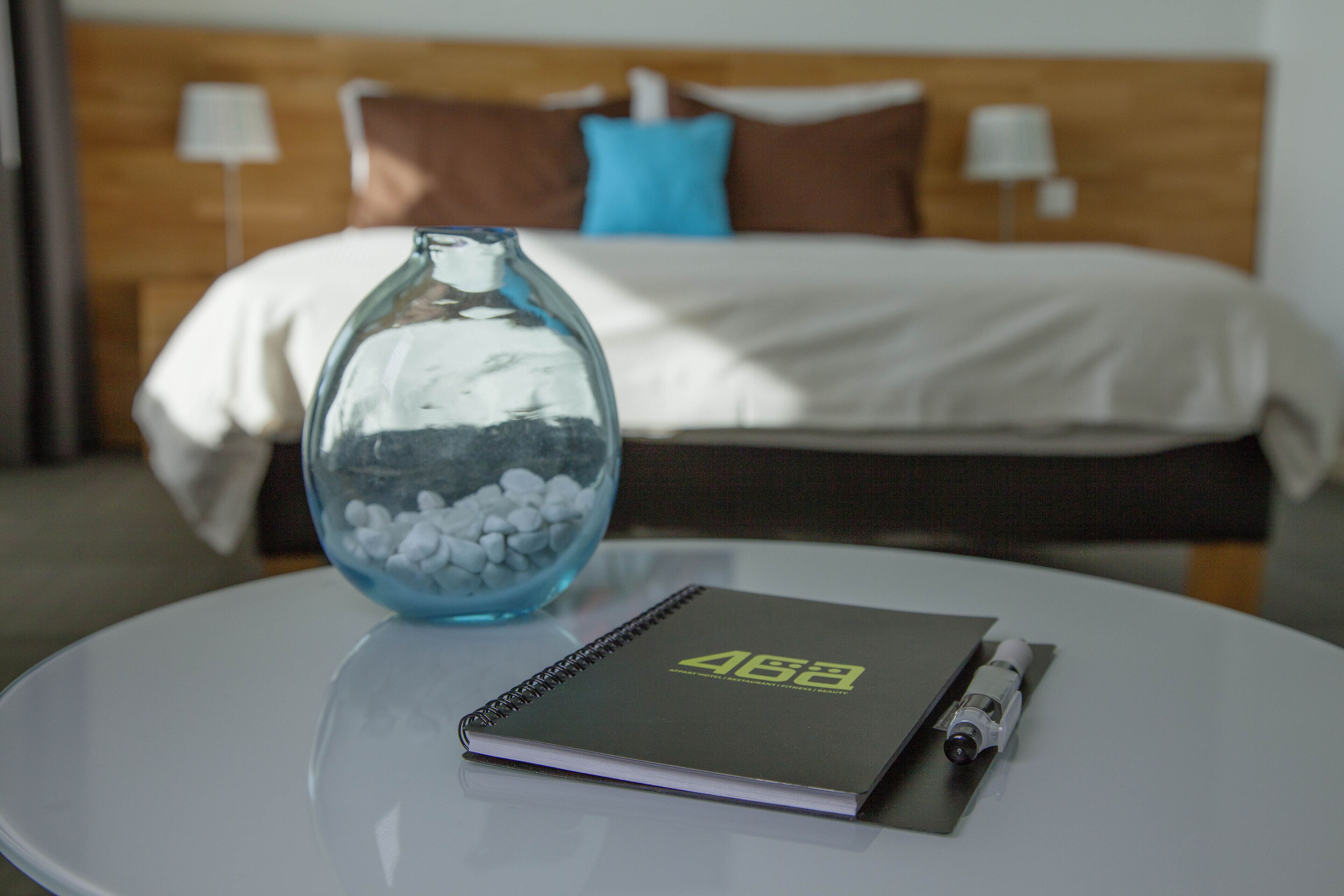 Ein Hotelzimmer mit Bett, Nachttisch, Notizbuch und einer Vase mit weißen Kieselsteinen.