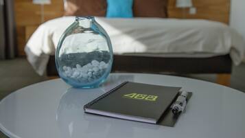 Ein Hotelzimmer mit Bett, Nachttisch, Notizbuch und einer Vase mit weißen Kieselsteinen.