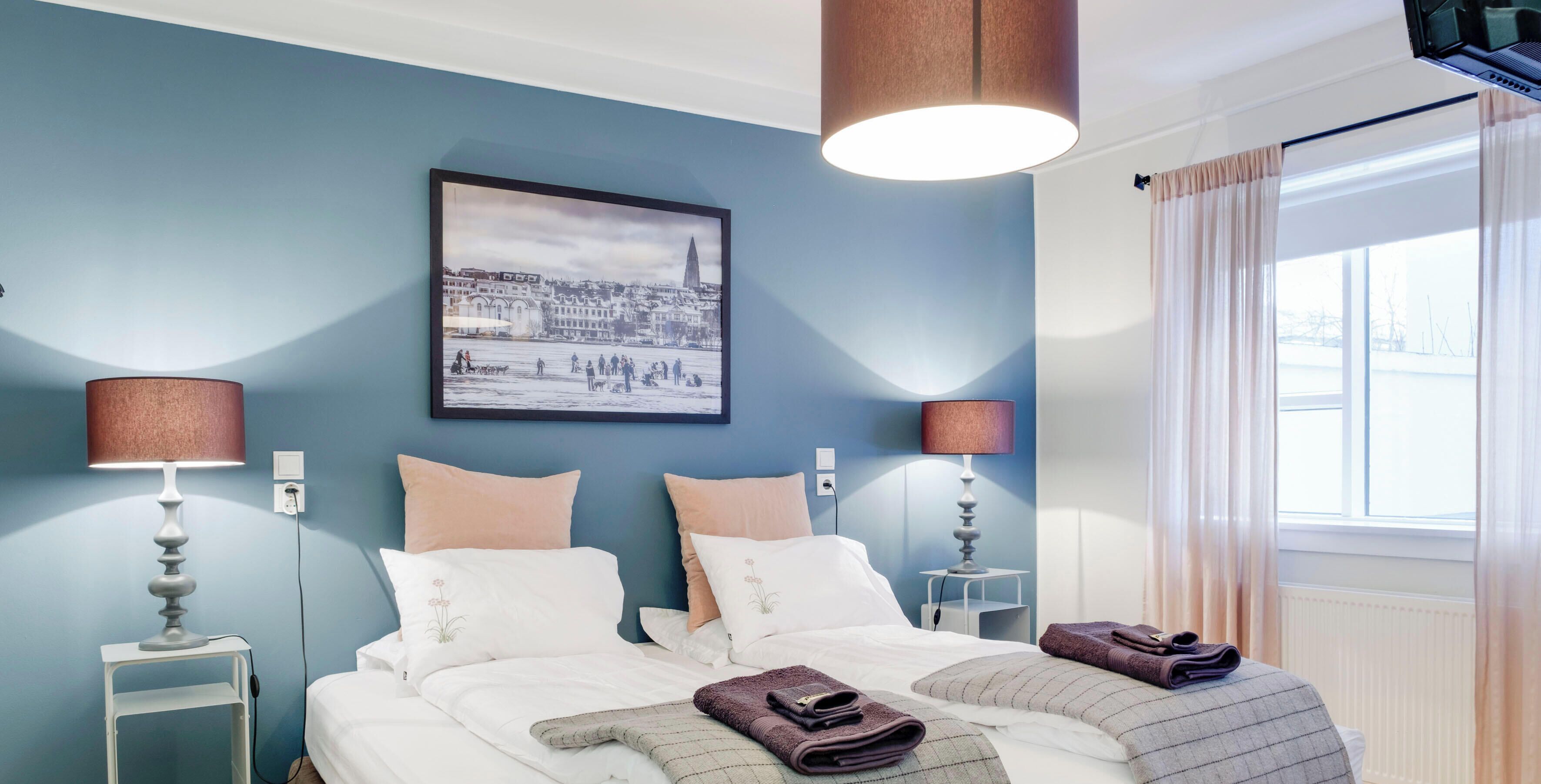 A hotel room with a bed, two bedside tables, lamps, a framed picture on the wall, and a window with curtains.