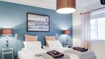 A hotel room with a bed, two bedside tables, lamps, a framed picture on the wall, and a window with curtains.