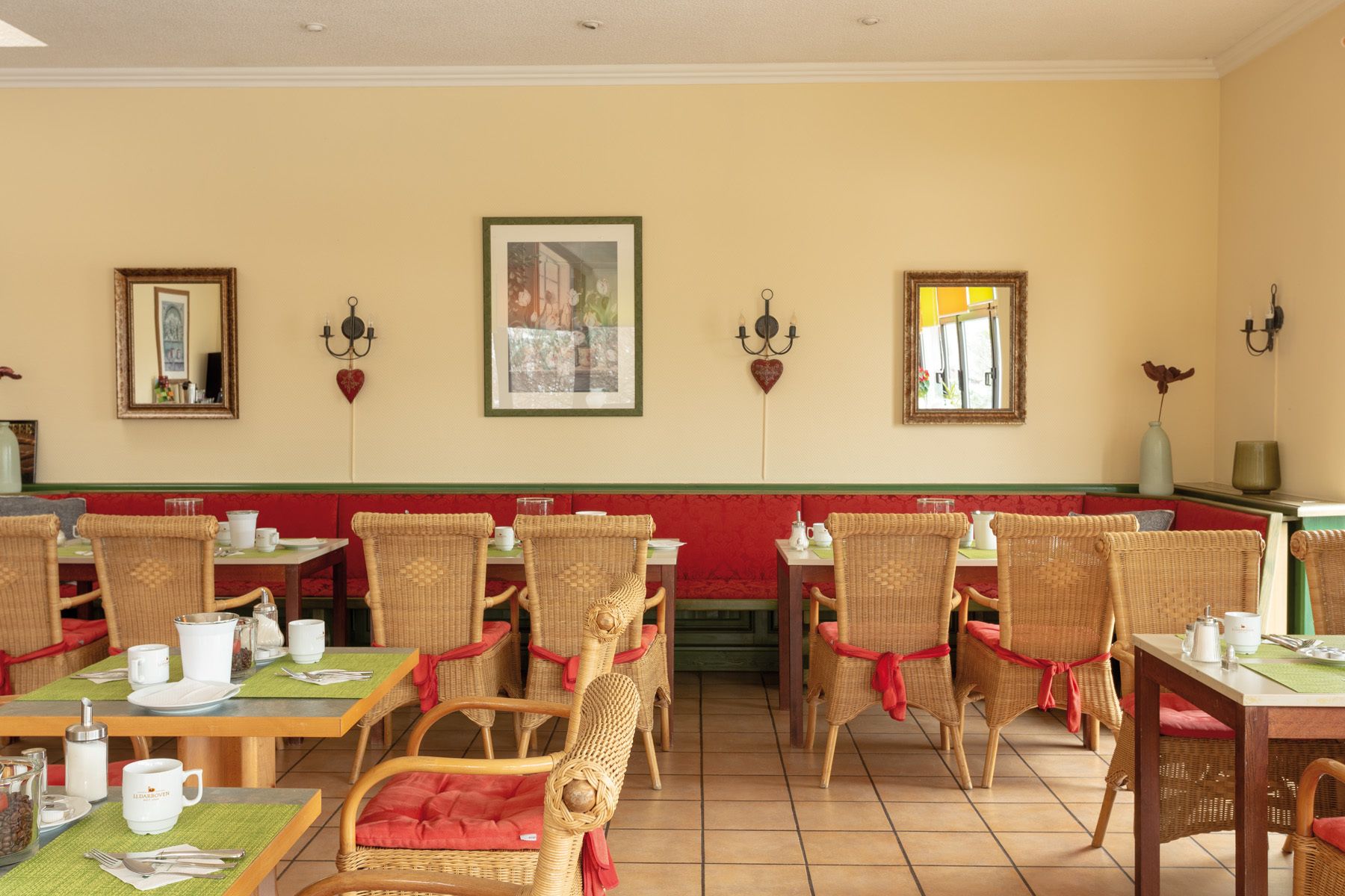 A dining area with wicker chairs, red cushions, and a green tablecloth.