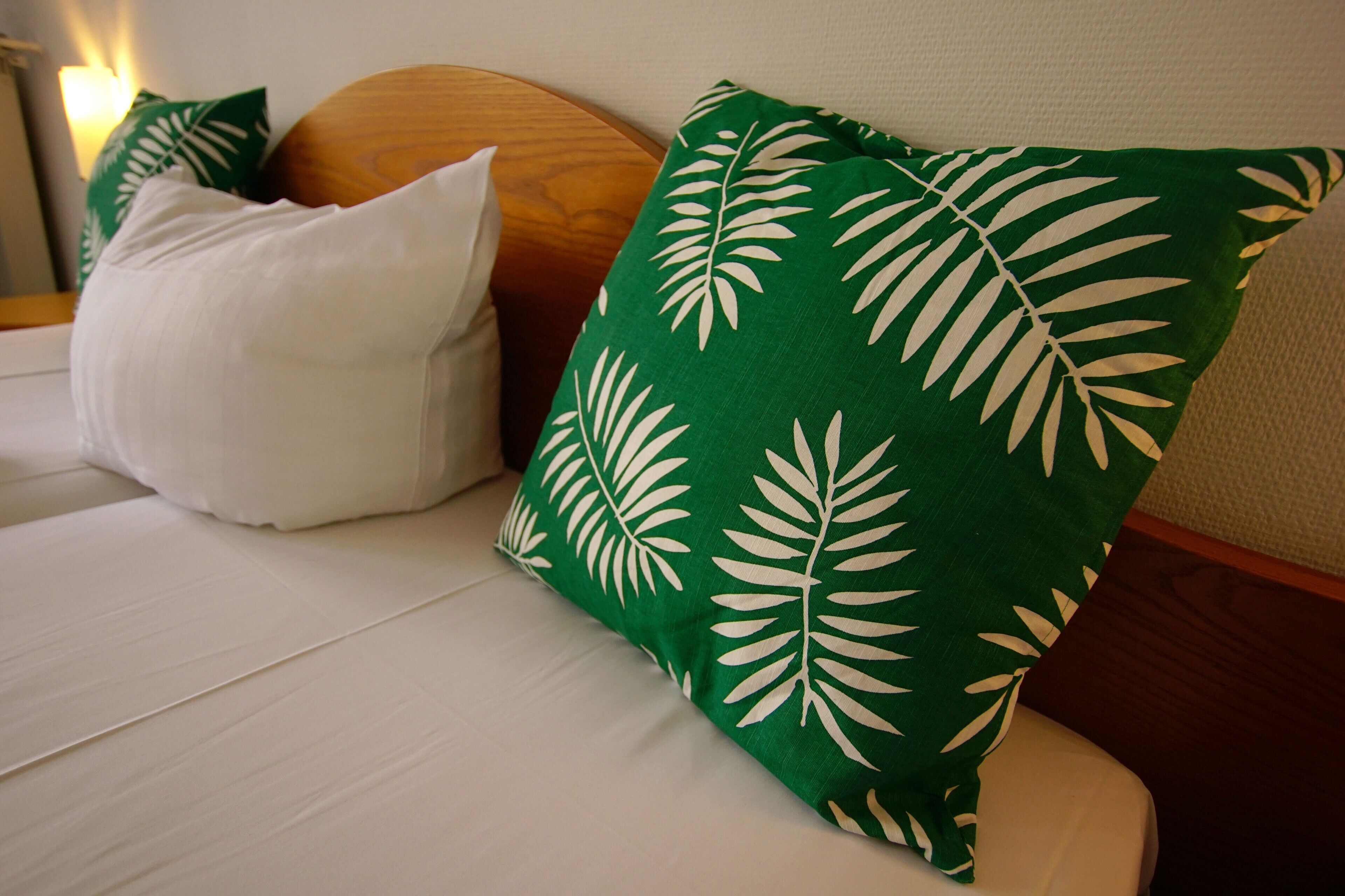 A bed with white bedding and two pillows, one green with a leaf pattern and one white.