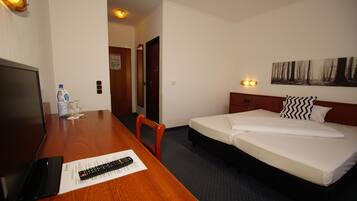 A hotel room with a wooden desk, a bed with white bedding, a painting on the wall, and a remote control on the desk.