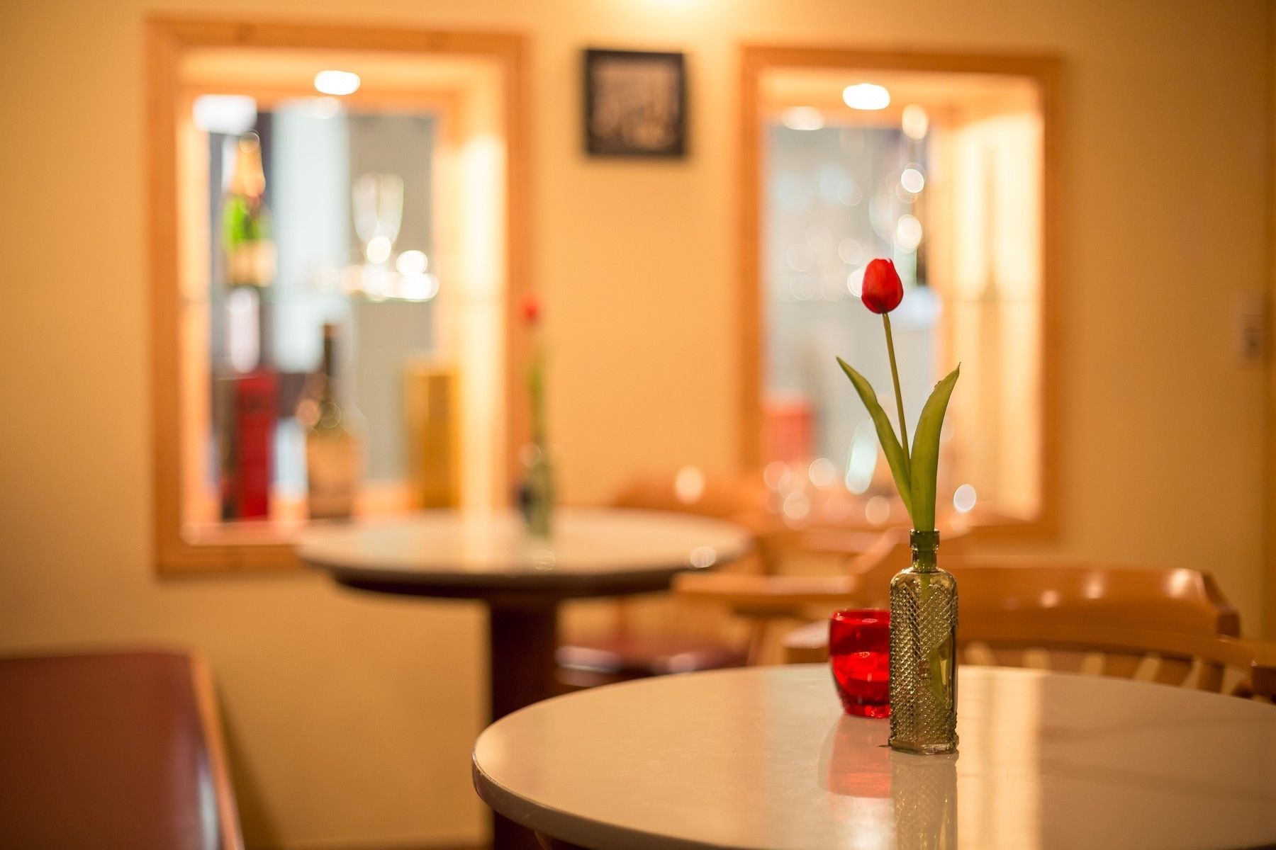 A dining area with a round table, a vase with a single red rose, and a textured glass candle holder.