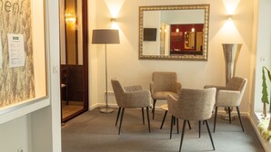 Een hotel lobby met een ronde tafel, vier stoelen, een grote spiegel en twee vloerlampen.