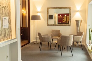 Um hall de hotel com uma mesa redonda, quatro cadeiras, um espelho grande e duas luminárias de chão.