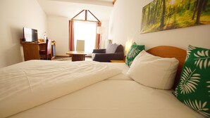 Een hotelkamer met een groot bed, een bureau met een computer, een stoel en een raam met gordijnen.