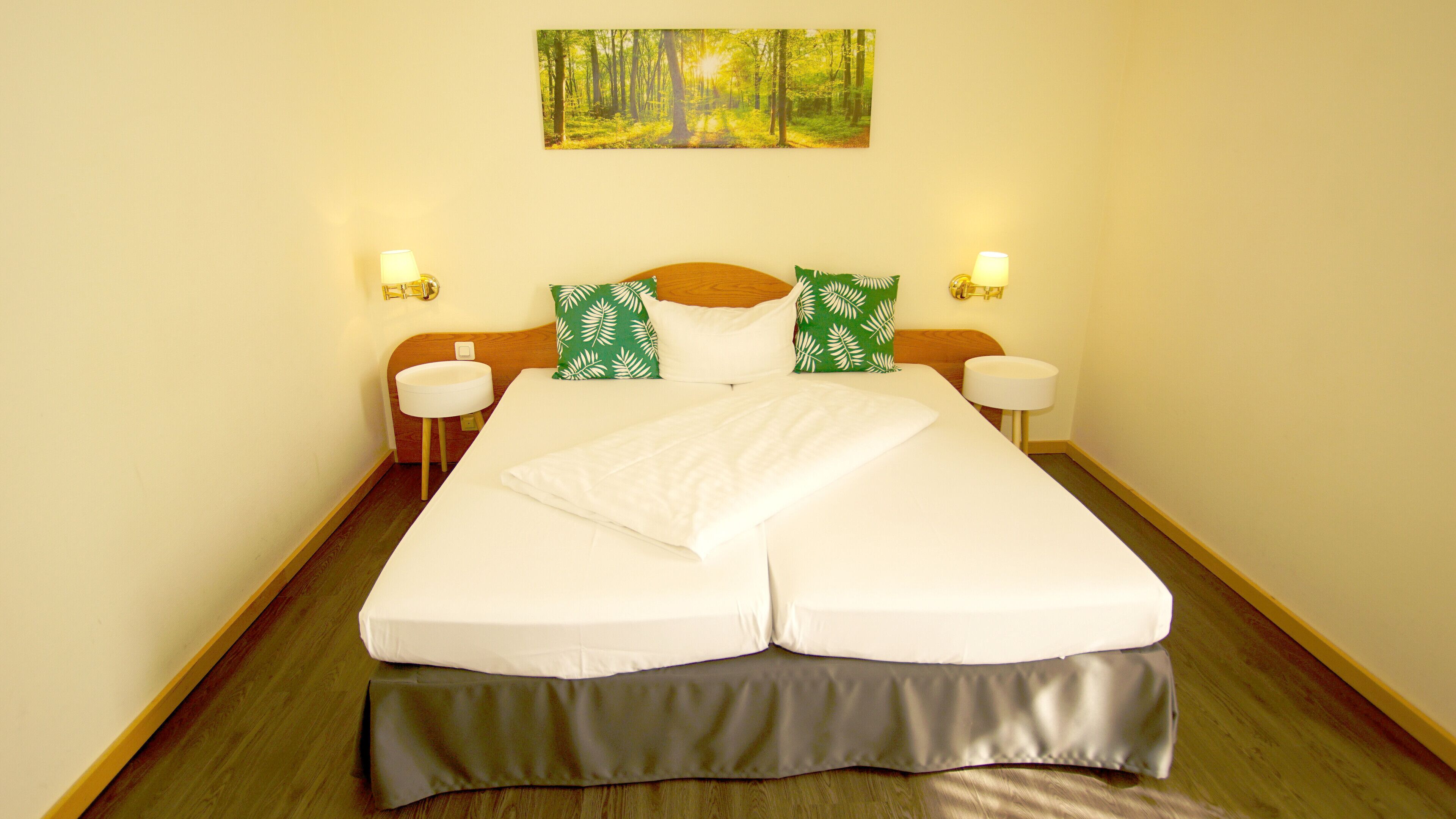 A hotel room with a large bed, two bedside tables, a wall-mounted painting, and a small bedside lamp.