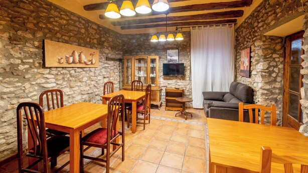 Un comedor rústico con mesas y sillas de madera, paredes de piedra y chimenea de piedra.