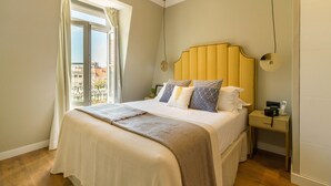 A bedroom with a large bed, a bedside table, a nightstand, and a window with curtains. - Bairro Alto Suites (Lisbon)