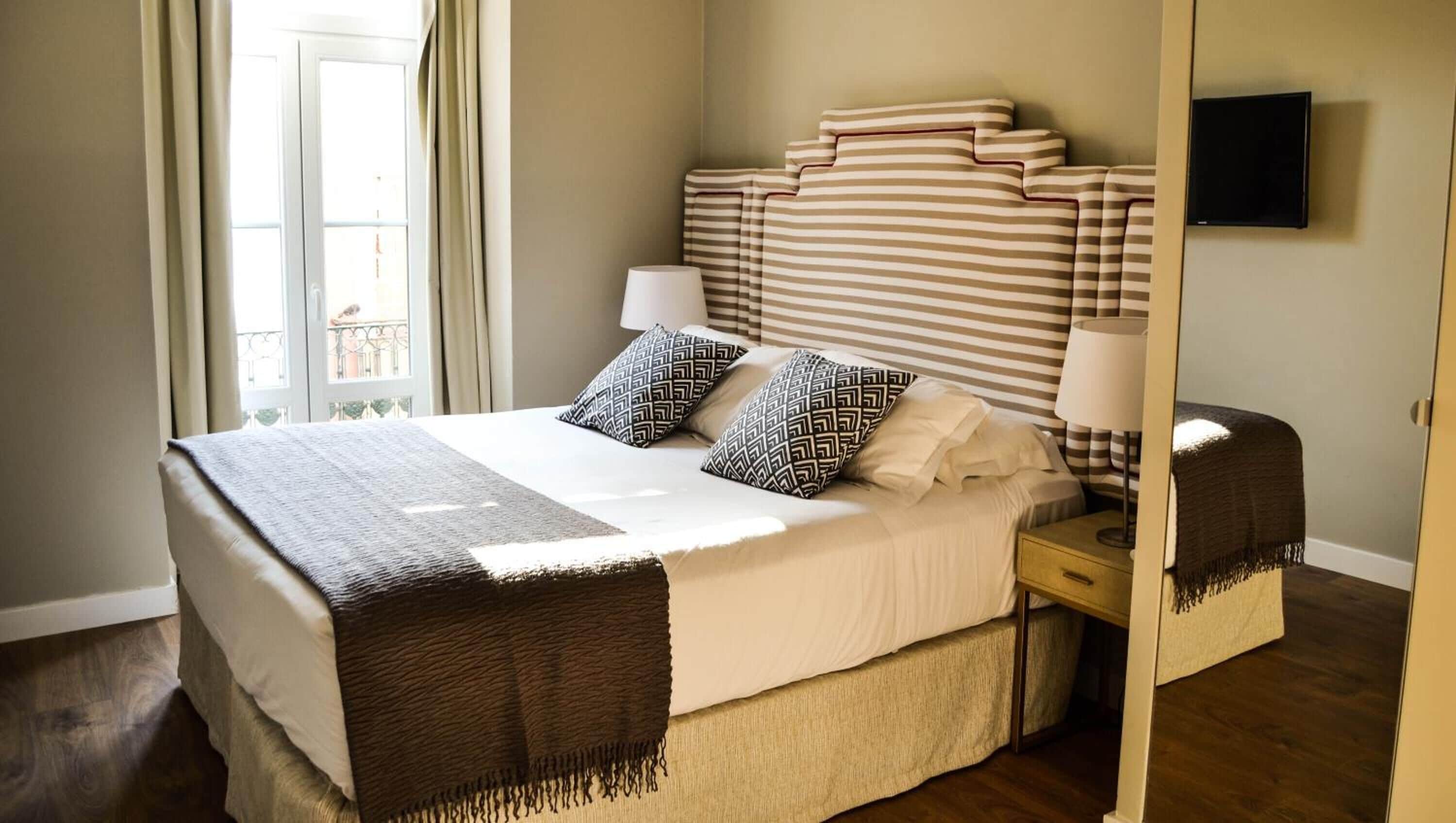 A neatly made bed with striped bedding, two patterned pillows, and a bedside lamp.