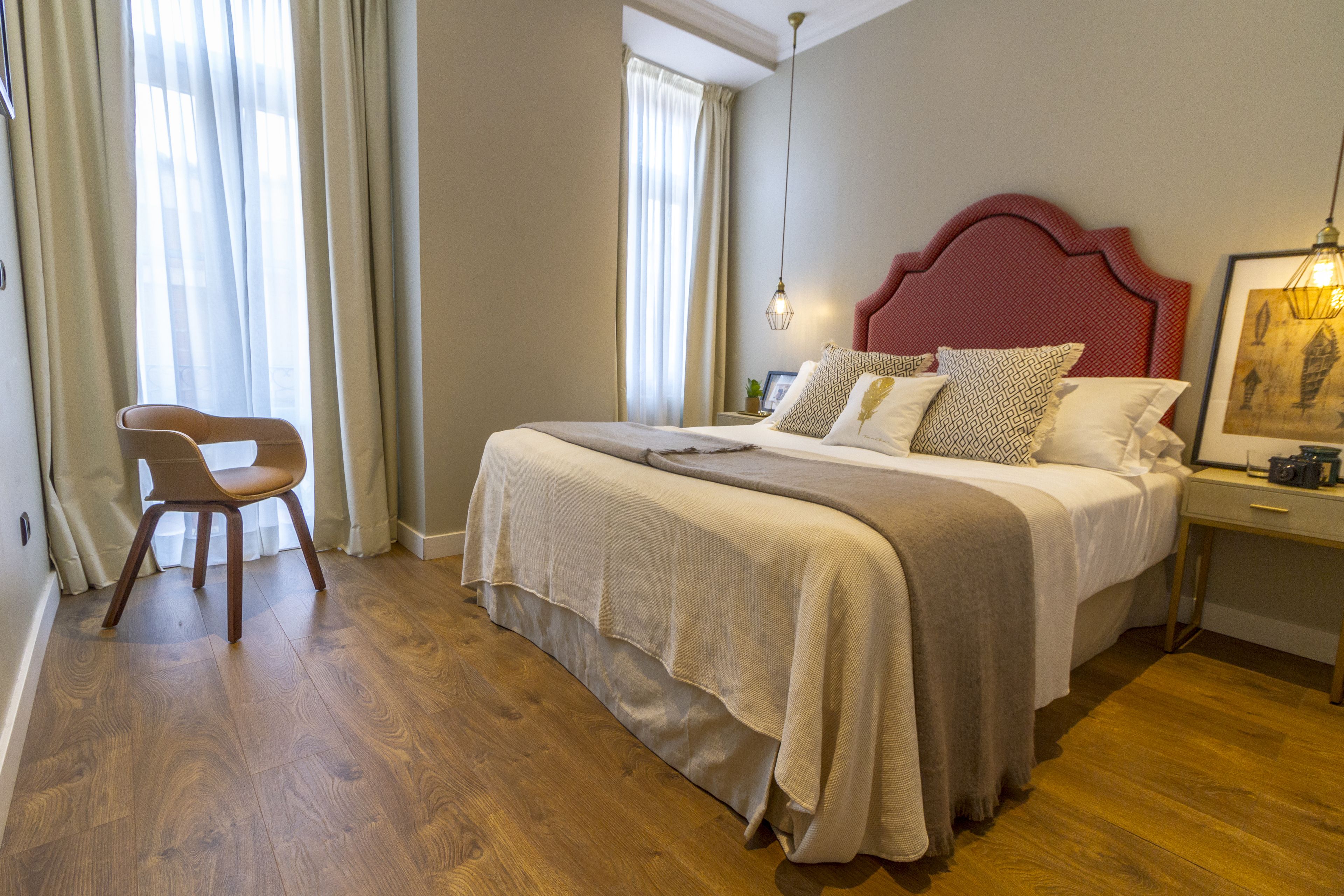 Een slaapkamer met een groot bed, een stoel, een nachtkastje en een raam met gordijnen.