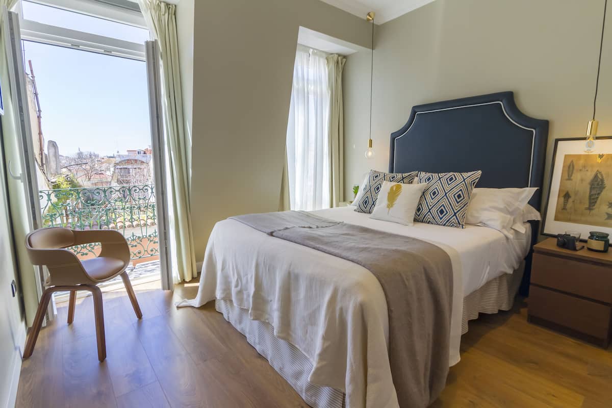 Une chambre avec un grand lit, une chaise, une table de chevet et une vue sur la ville par une fenêtre.