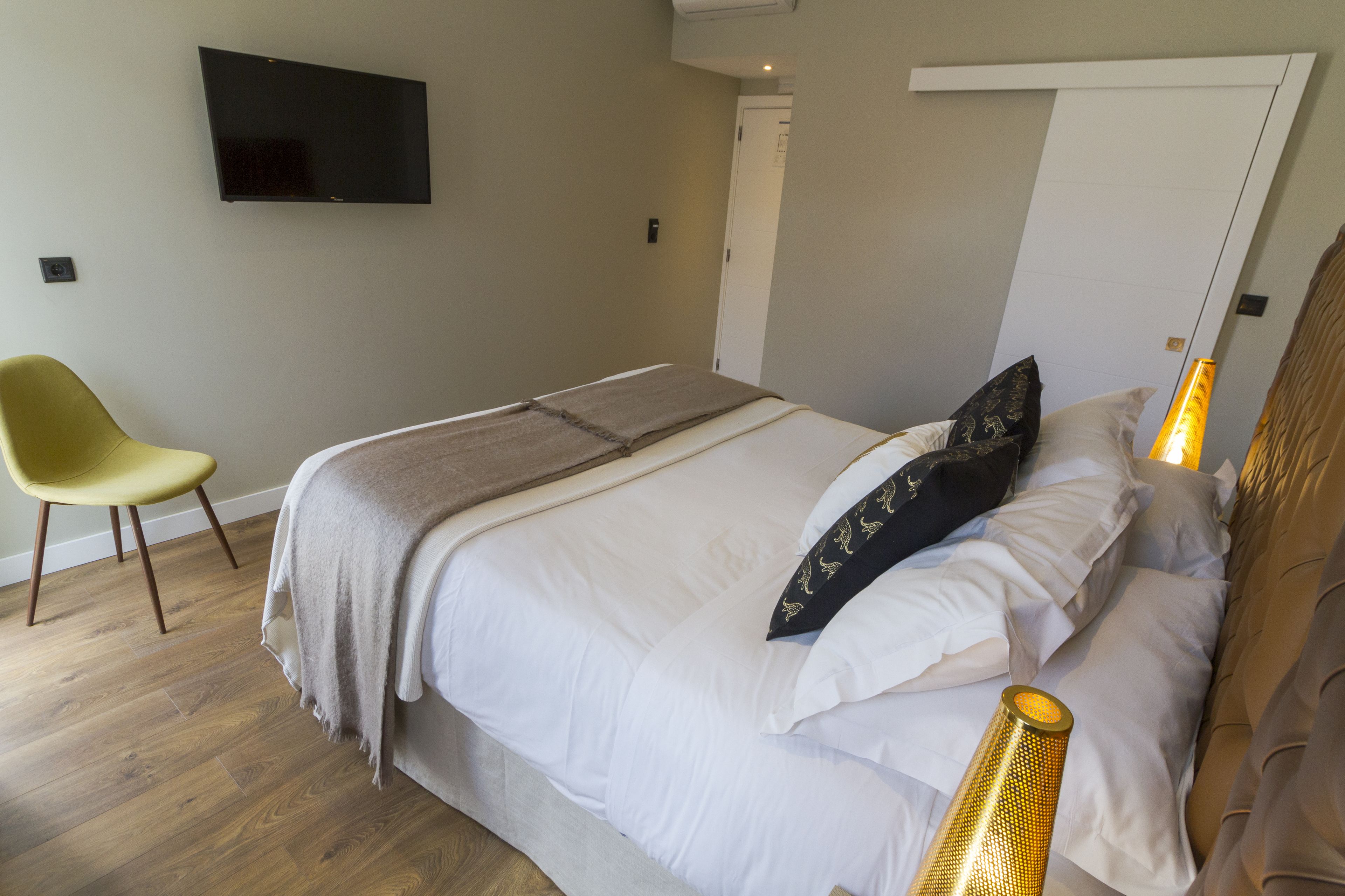A bedroom with a bed, a TV mounted on the wall, a chair, and a door.