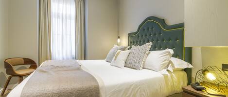A neatly made bed with a green headboard, a bedside lamp, and a chair.